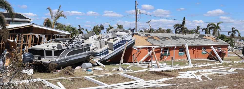 An image of hurricane damage in Florida of a red home with a boat on the lawn