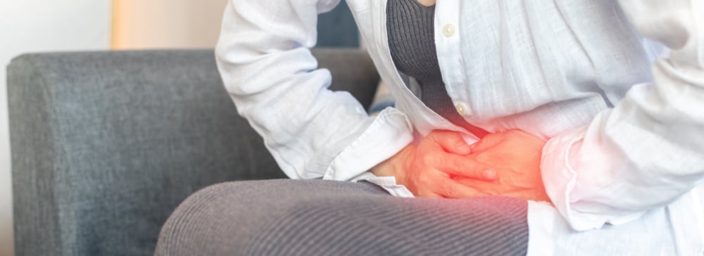 A person grasping their stomach in pain while sitting on a couch