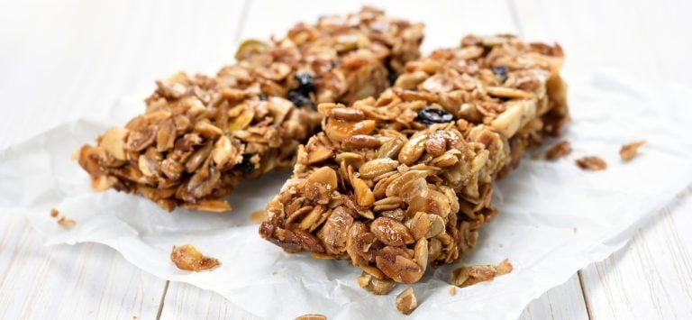 Two granola bars on white wax paper sitting on a wooden table