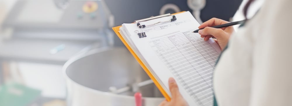 Woman with a clipboard checking quality of food in a commercial kitchen