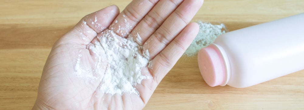 Baby talcum powder on hand with a talcum powder bottle on the table