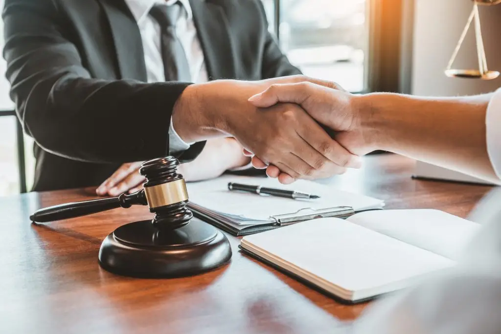 Two people shaking hands over documents and a gavel on a desk