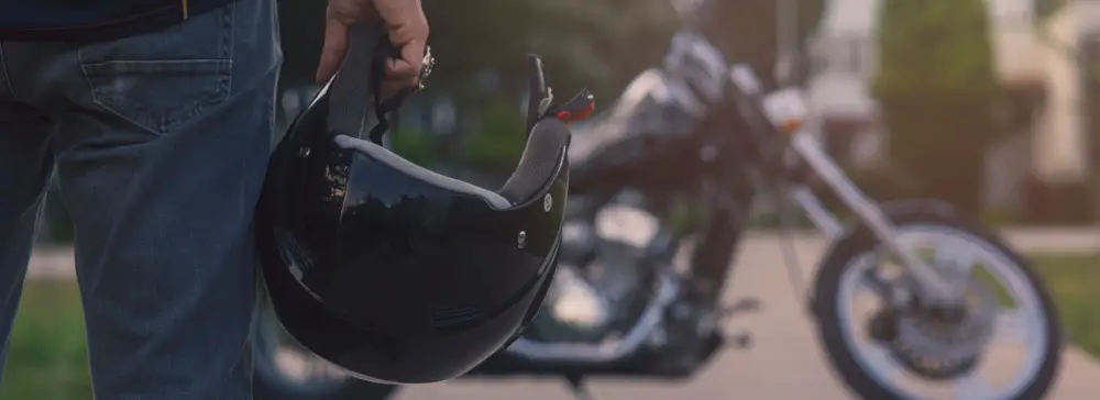 Motorcycle rider holding a helmet facing a black motorcycle