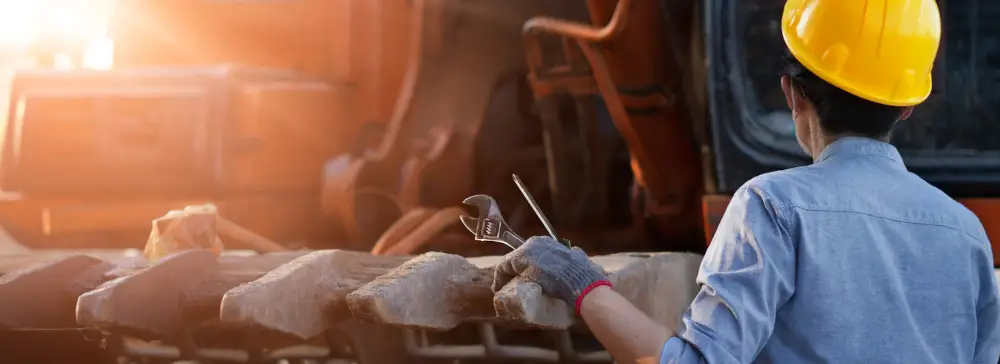 A construction worker in a hard hat with a wrench in front of a front end loader