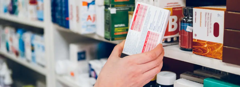 Un farmacéutico tomando una caja de medicamentos de una estantería