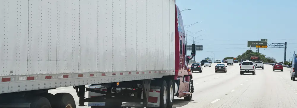A red semi-truck driving down the highway in Florida with a sign for Linton Blvd ahead