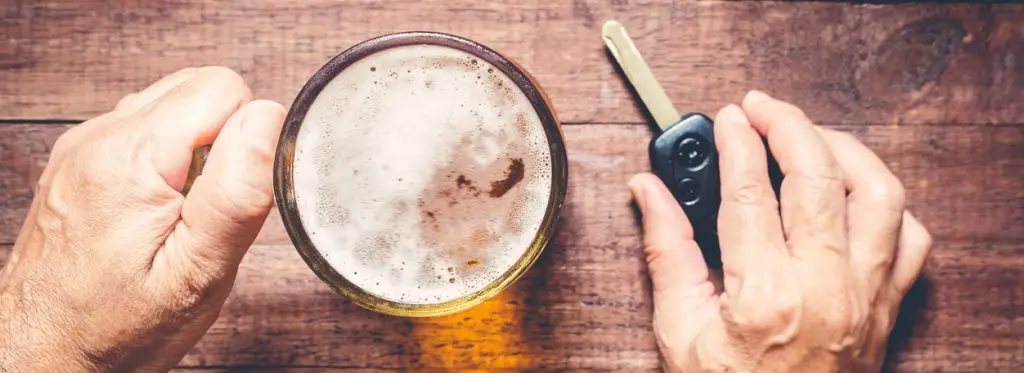 Manos de un hombre sosteniendo un vaso de cerveza y las llaves del coche